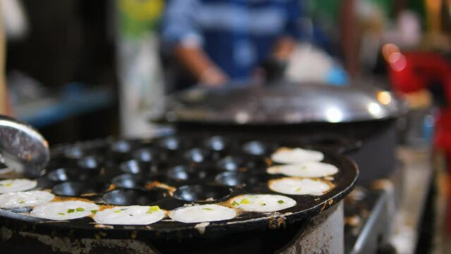 Asian street food: traditional Thai Kanom Krok dessert coconut-rice pancake cooked in a special pan with half-spherical molds, high quality 4K slowmotion hedonism travel concept footage, Thailand.