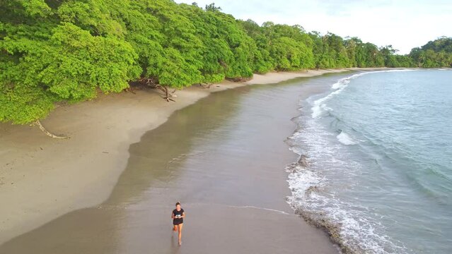Young caucasian female tourist jogging over tropical beach in national park of Marino Ballena, Costa Rica.