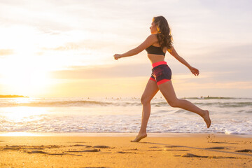 Fototapeta na wymiar Fit woman jogging along a beach during sunset