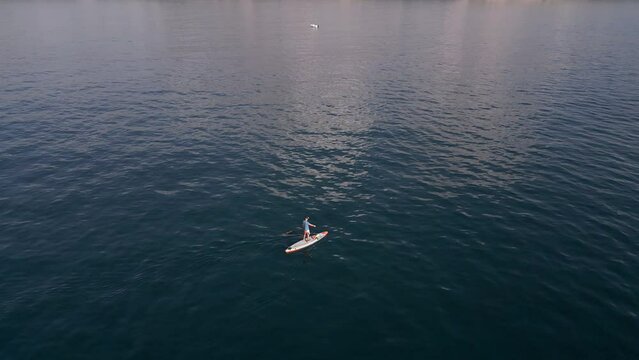 Aerial view of a man paddling a stand-up paddleboard or SUP board on a calm sea.