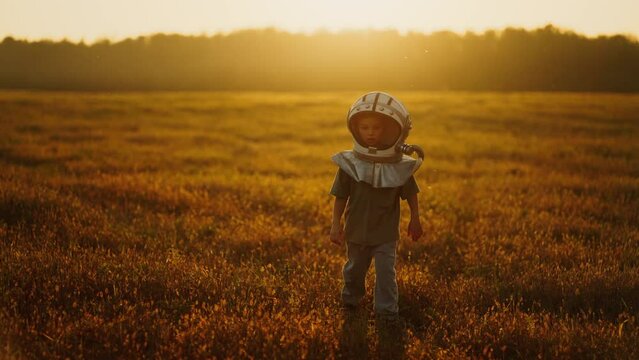Child Boy Imagine Himself As Astronaut On Mars, Walking In Field In Summer, Wearing Space Helmet