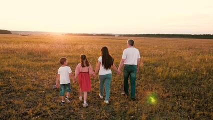 Fototapeta na wymiar Positive parents with little children walk joining hands across sunset field