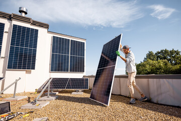 Man carries solar panel while installing solar plant of a rooftop of his property. Wide angle view. Renewable energy for self consumption concept. Idea of installing panels for households