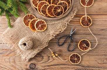 New Year's garland made with your own hands from dried orange slices on a wooden rustic table. Top view. Winter holiday concept. - obrazy, fototapety, plakaty
