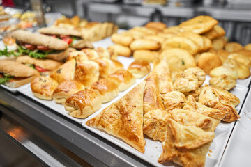 Fresh sandwiches, pies and pizza to choose from in the window of a cafe, buffet or self-service cafe. Croissant with ham and cheese. Hot pastries lie on the shelf in the cafe. Buns in the store. © malkovkosta