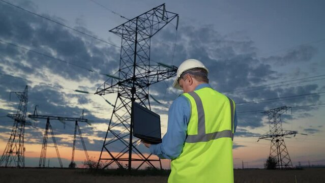 Engineer checks equipment with laptop walking to power transmission lines