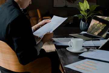 Close up rear shot young woman working with business plan on desk. Concentrated businesswoman checking graphs. Analyzing fund investment. Girl holding diagram documents