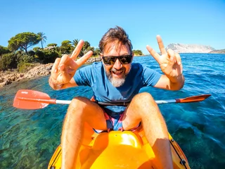 Fotobehang One cheerful man have fun and pose for a crazy picture sitting inside a yellow kayak canoe  with ocean water and coast in background. Happy tourist summer holiday vacation lifestyle people doing tour © simona