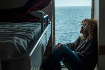 One woman passenger inside cabin boat cruise ferry having relax sitting near the window with ocean sea in background outside. Bedroom indoor leisure activity. People and travel concept. Vacation. - obrazy, fototapety, plakaty