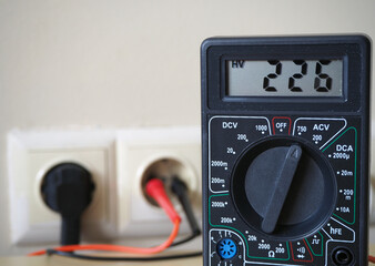Voltage at electrical outlets. Mains electricity measurement. Controlling with digital voltmeter.