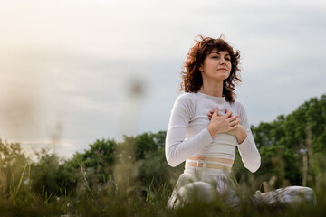 Lady practicing diaphragmatic breathing in the morning. Sports woman doing yoga deeply inhale. Girl hands touch chest training on yogamat outdoors. Professional pranayama master class - obrazy, fototapety, plakaty