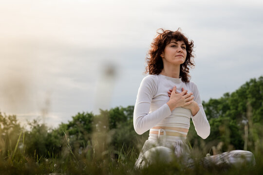 Lady practicing diaphragmatic breathing in the morning. Sports woman doing yoga deeply inhale. Girl hands touch chest training on yogamat outdoors. Professional pranayama master class
