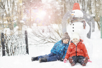 Children in the park in winter. Kids play with snow on the playground. They sculpt snowmen and slide down the hills.