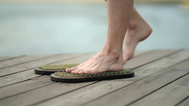 Yoga girl standing with her bare feet on a board with sharp nails on a wooden pier on a summer day