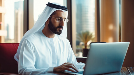 Portraits of a successful businessman in traditional emirates white dress, Arab man working in his business office of Dubai using laptop.