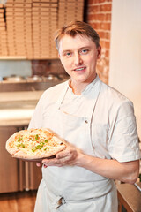 The chef holds a pizza in his hands. Neapolitan pizza from a wood-fired oven. Pizza is on the plate. Pizza with pear and gorgonzola. Fast delivery of food. 