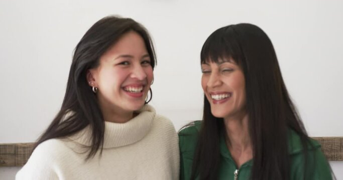 Portrait of happy biracial mother and adult daughter smiling together at home, slow motion