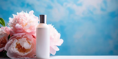 Foto op Canvas Mock up of natural, flower beauty product. White cosmetic bottle with two beautiful, pink peonies on a blue background with copy space. © Coosh448