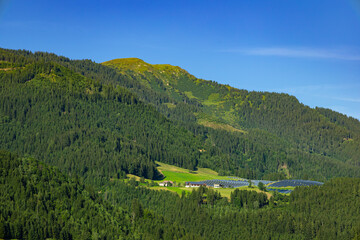 view of solar panels in the green mountains of Austria on a sunny summer day against a blue sky.