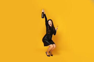 Girl with champagne and glasses on a yellow background. - obrazy, fototapety, plakaty