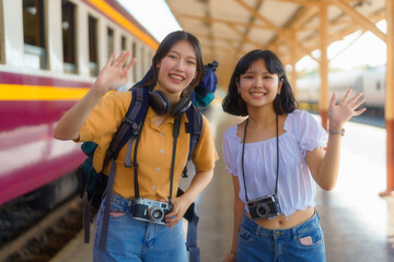 Two Asian female tourists are expressing their joy at reaching their destination on the platform of a train station.