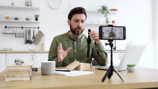 Good-looking interested in technology guy pointing out at favorite waterproof sports watch while recording video on mobile camera. Creative vlogger telling subscribers about best present for men.