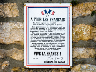 Close-up of an enamel sign showing the poster "A Tous Les Français" by General de Gaulle, following the Appeal of 18 June 1940, screwed on a stone wall.