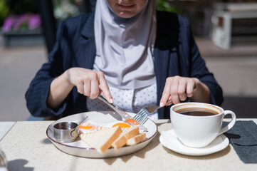 Caucasian woman in hijab having breakfast in outdoor cafe. 