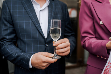 A stylish man in a blue checkered jacket holds a glass of champagne, wine in his hands at a banquet, party. Food photography.