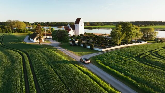 Aerial view following a car arriving at a church, summer sunset on the countryside