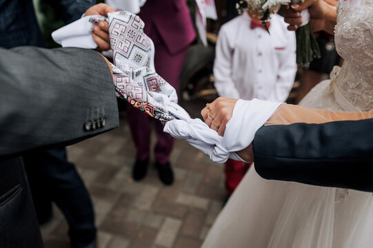 The bride and groom stand at the ceremony with an embroidered towel tied in a knot on their hands. Wedding photography, Ukrainian tradition, ritual, portrait.