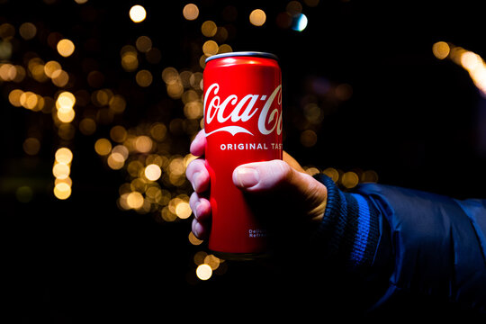 Coca Cola can in hand with Christmas lights and decoration in background shot at night in Belgrade, Serbia. Illustrative editorial image