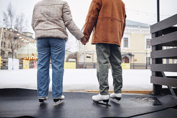Back view of couple holding hands in ice skating rink enjoying winter date, copy space