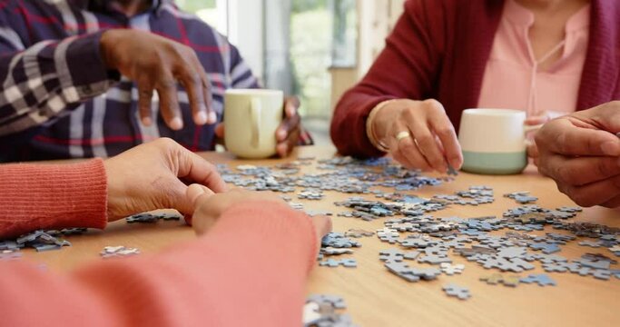 Midsection of diverse senior friends having coffee doing jigsaw puzzle at dining table, slow motion