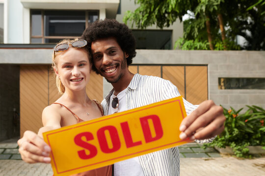 Exited new house owners holding sold sign board
