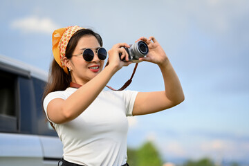 Smiling young woman taking photos with vintage retro camera during road trip on beautiful summer day