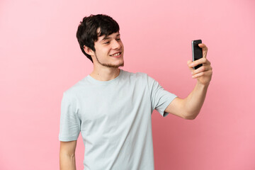 Young Russian man isolated on pink background making a selfie