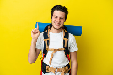 Young mountaineer Russian man with a big backpack isolated on yellow background showing and lifting a finger in sign of the best