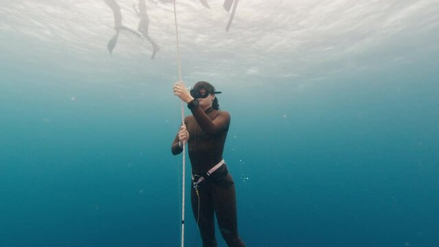 Confident woman freediver ascends along the rope during free diving training in the sea