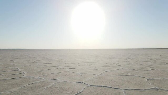An intense low angle eternity drone shot above the salt flats flying towards the sun and horizon.