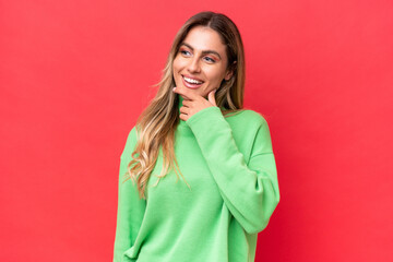 Young Uruguayan woman isolated on red background looking to the side and smiling