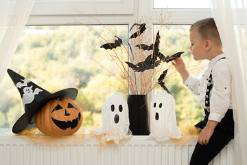 Halloween. Concept. A cute and cheerful boy sits near the window against the background of white...