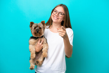 Young Lithuanian woman holding a dog isolated on blue background points finger at you with a confident expression