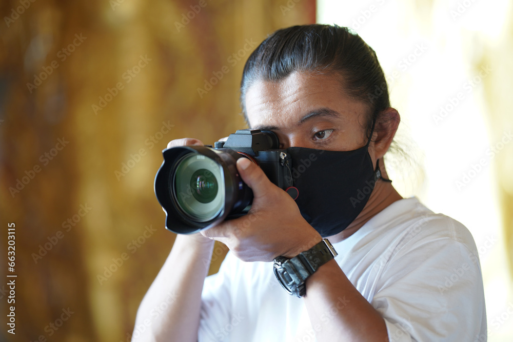 Wall mural A man wearing black mask is shooting photo through a viewfinder camera with the right eye.