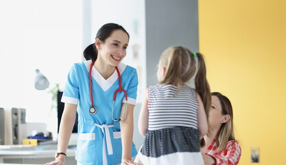 Portrait of pretty pediatrician chatting with cute patient child girl on appointment in clinic. Mum support daughter during visit to doctor. Health concept