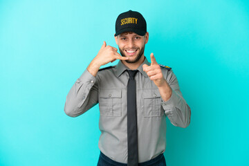 Young security man isolated on blue background making phone gesture and pointing front