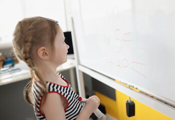 Fototapeta na wymiar Portrait of toddler writing solution of sums on white board at school, educational process. School kid think while doing mathematics problem. Learn concept