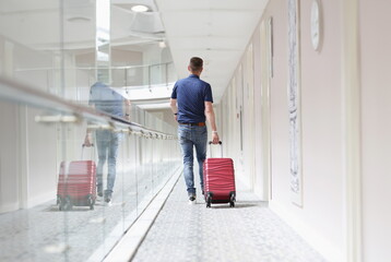 Low angle of young male pulling red luggage behind, search for his room in hotel building....