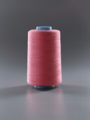 Close-up of thread for dressmaking, pink colour thread spool on grey surface, yarn for sewing....