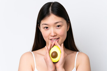 Young Chinese woman isolated on white background holding an avocado while smiling. Close up portrait